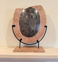 Front view of marble display plate showing pink border and dark veined center on metal stand