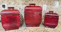 Three red ceramic canisters with lids on countertop