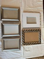 Five small picture frames laid out: three silver-tone rope-edge, one white with silver balls, one metallic twisted-rope