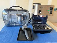 Front view of Starbucks Barista espresso machine alongside accessory kit case, portafilter and drip tray