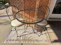 round metal glass-top bistro table with two chairs and rug