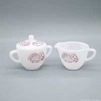 Front view of milk glass lidded sugar bowl and creamer showing burgundy floral print