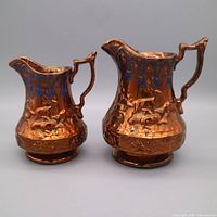 front view of both copper-lustre creamers showing decoration and size difference