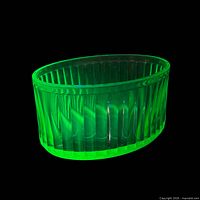 Dish glowing green on black background showing uranium fluorescence