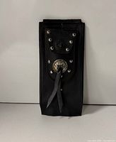 Front view of black leather tank bib showing pouch, rivets, concho and tassel