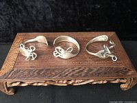 Three fork bracelets displayed on carved wooden stand