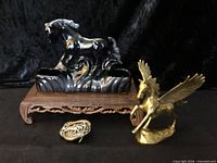 Group shot showing ceramic horse pen stand on wooden riser, brass Pegasus figurine, and bronze belt buckle