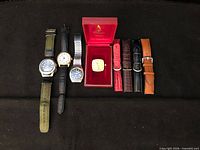 Group shot of four watches, watch head in red case, and five leather straps