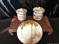 Front view of two lidded Kutani cups and saucer