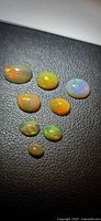 Eight oval cabochon opals displayed on black surface showing play-of-colour