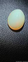Opal cabochon on black textured background, showing translucence and slight color flash