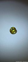 Round greenish-yellow faceted sphene on neutral background