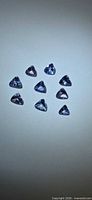 Nine loose trillion-cut violet-blue tanzanite stones arranged on neutral background