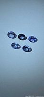 Five loose oval violet-blue gemstones on white background