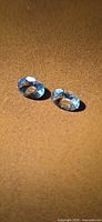 Two faceted light blue oval gemstones on brown surface