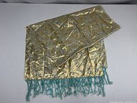 Gold brocade scarf with aqua fringe laid flat