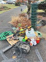 Overall lot piled at driveway showing pressure washer, blower, hose, roll of fence and assorted tools