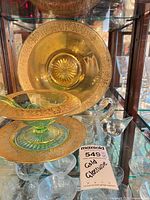 Amber gilt-rimmed plate, green compote with ladle, clear swan displayed together in cabinet