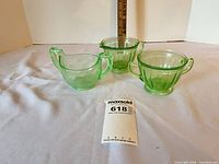 Three light green uranium glass pieces: two creamers and one sugar bowl on white surface with ruler for scale