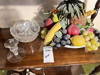 Lot overview showing cut-glass bowl, glass candlestick and faux fruit centerpiece on plate