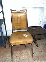 Front view of mustard vinyl chair, white laminate tabletop leaning behind, pedestal base visible