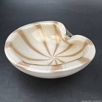 Oblique view showing white glass body, gold spiral stripes, free-form rim