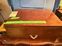 Closed wood storage chest with brass handle and note on missing spoon