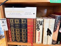 Shelf with classic and fiction hardcovers including Queen Elizabeth biography, The Stand and gilt leather-bound editions