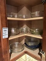 Cabinet view showing multiple glass bowls, casseroles and lids on three shelves