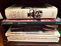 Stack of eight hardcover books on shelf showing spines and titles