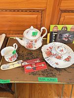 Full view of teapot, creamer, covered sugar on plate, souvenir spoons and partial postcards