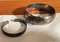 Floral engraved hinged bangle and plain cuff side by side