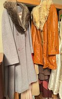 Grey wool coat and caramel leather coat hanging side by side, fur collars visible