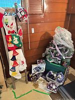 Tree wrapped in plastic, green bin, wood ladder with felt decorations, assorted ornaments at base