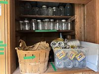 Cupboard shelves holding numerous glass mason jars, plastic tote with metal lids, and wood basket