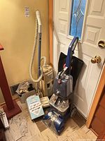 Electrolux vacuum, Hoover carpet cleaner, filter-bag box and attachments grouped by doorway
