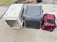 Front view of three pet enclosures lined up: hard plastic crate, gray soft carrier, maroon soft carrier
