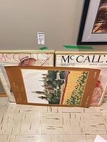 Three framed posters leaning against wall: two McCall's covers and Canada tourism poster