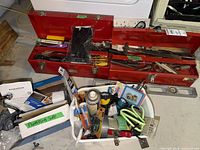 Open red toolboxes with hand tools and white bin of consumables