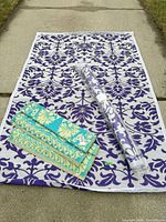 Overview of three outdoor rugs/mats displayed: large purple-white laid out, smaller turquoise folded, rolled purple-white in plastic