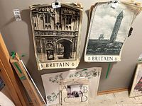 Stack of Britain travel posters hanging, adjacent rolled tubes and decorative board visible