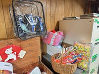 Shelf area showing clear vinyl bag of yarn, box of pink skeins, wicker basket of packaged needles