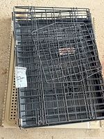 Collapsed black wire crate stacked on beige plastic kennel parts
