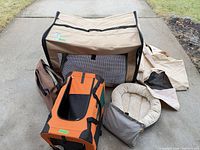 All three items grouped: tan Canine Camper playpen, orange Pet Life carrier, tan bolster bed