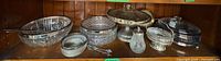 Shelf view of entire lot showing glass bowls, metal compote, covered dish, shaker, basket and spoons