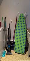 Group shot of ironing board, vacuum, mop, broom and other tools