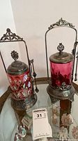 Two cranberry glass pickle castors in silver-plate frames on table