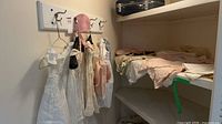 Overview of hanging white infant garments, pink bonnet, shelf with blankets