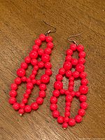 Front view of both neon pink beaded earrings on wood surface