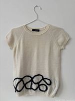 Front view of cream short-sleeve sweater with black loop design